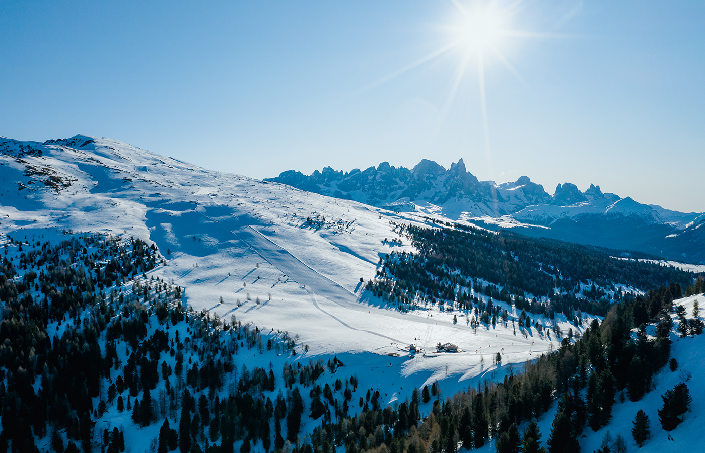 	Winterpanorama mit verschneiten Hängen und sonnenbeschienenen Dolomiten	