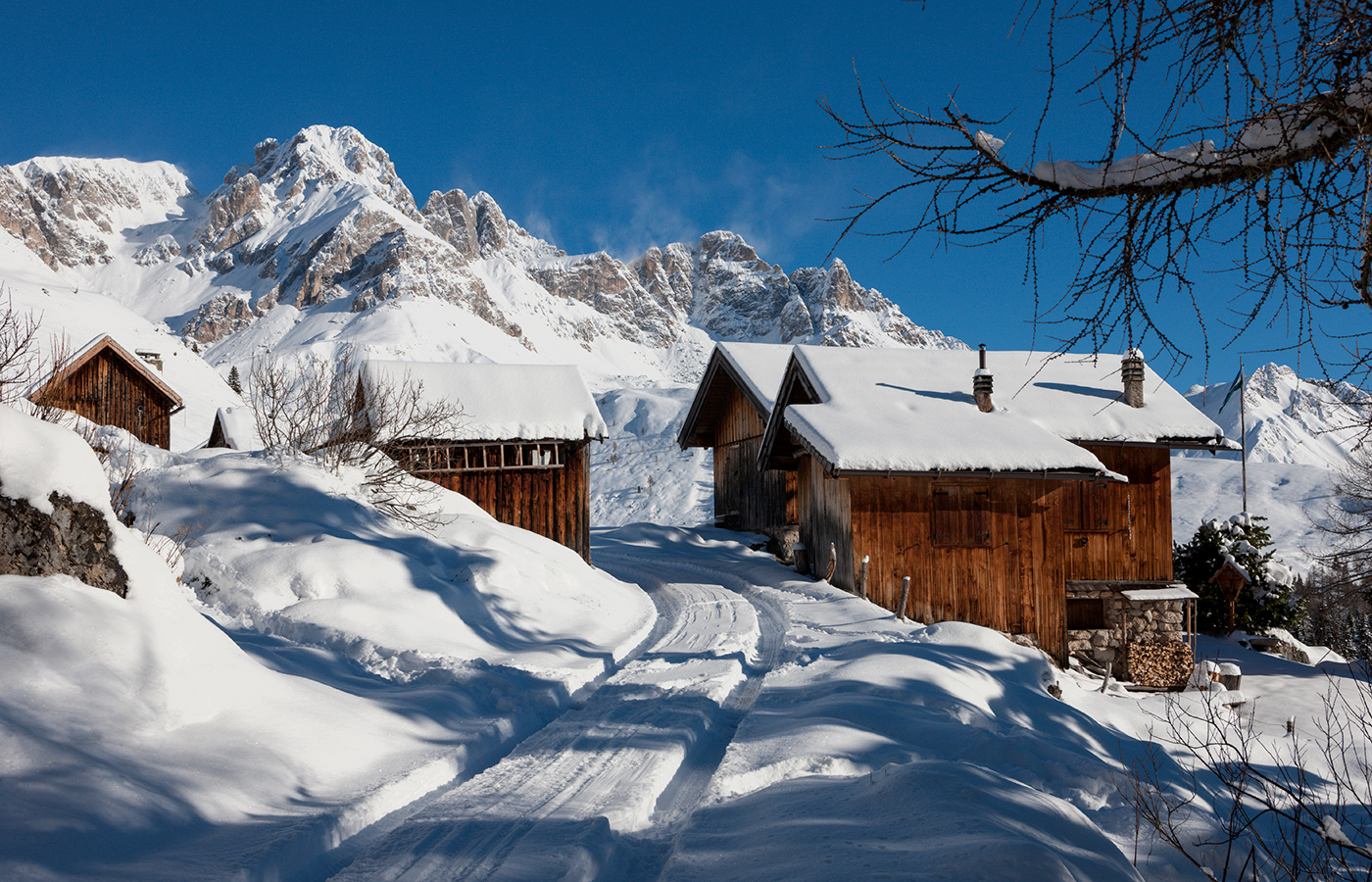 	Holzhütten in einem verschneiten Alpendorf mit Dolomiten im Hintergrund	