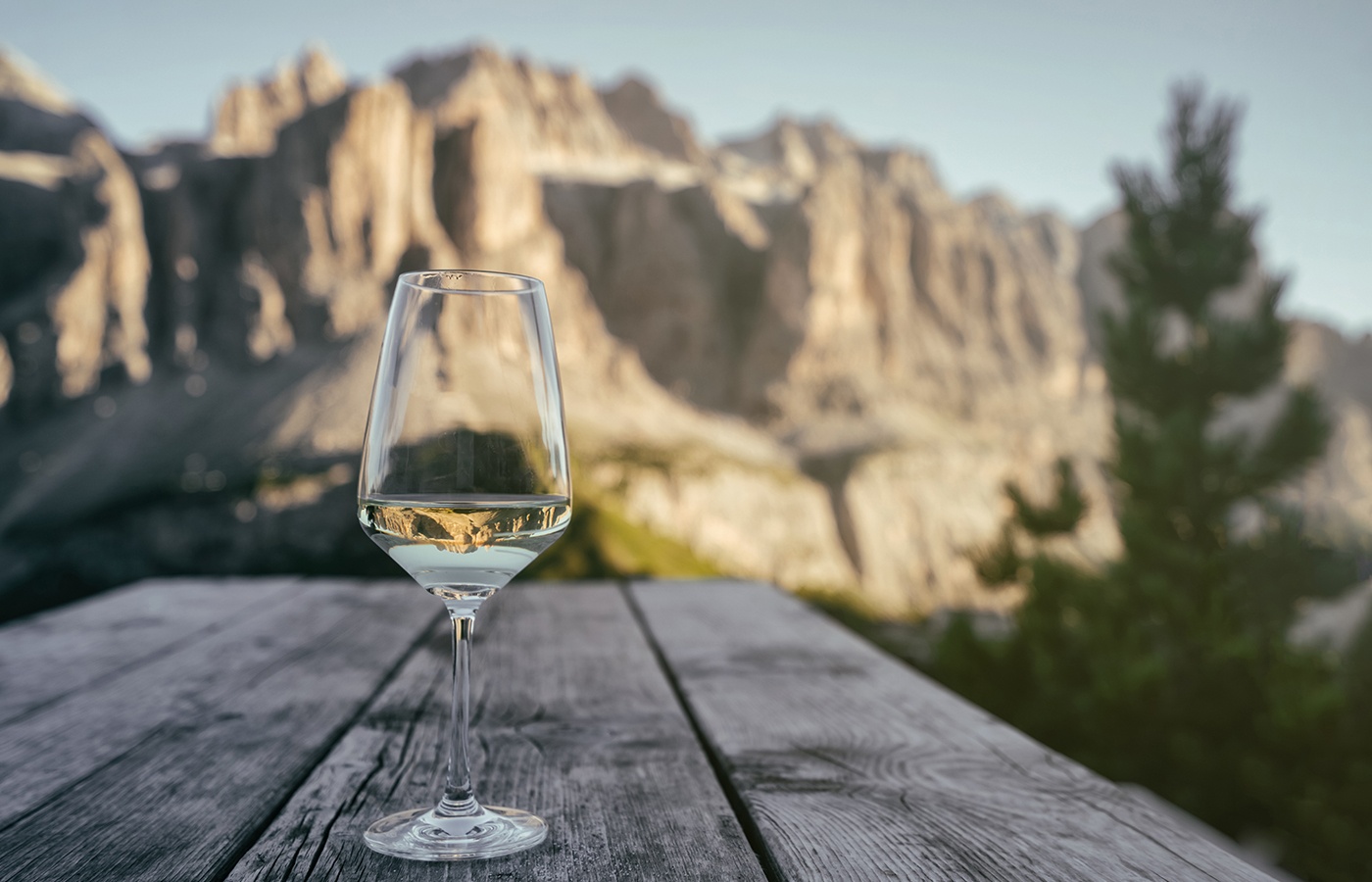 Glas Weißwein auf Holztisch mit Dolomitenblick.